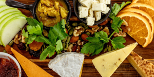 Cheese board with oranges, cheese, apples and greenery.